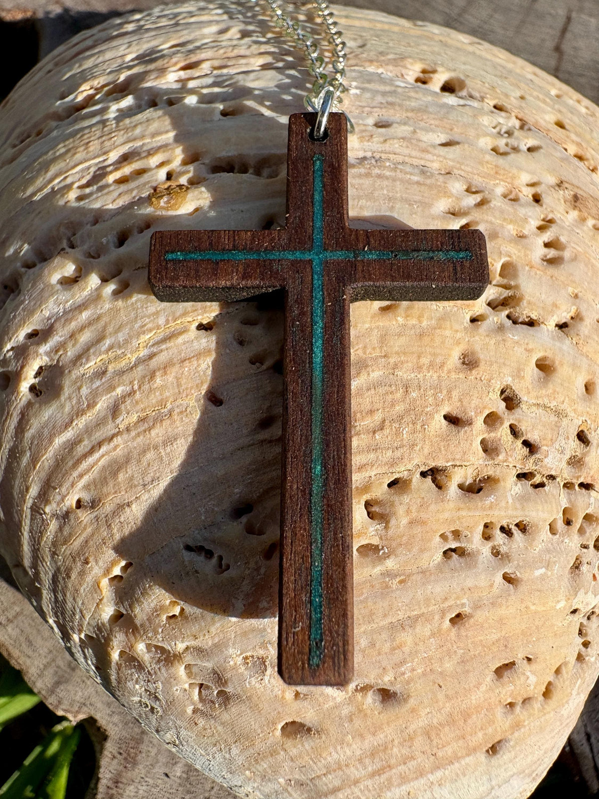 Black walnut cross necklace with turquoise resin inlay and silver-colored chain on a pale seashell