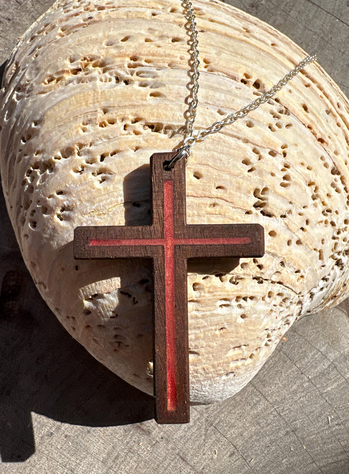 Red resin-inlay walnut cross necklace and silver-colored chain draped over a seashell