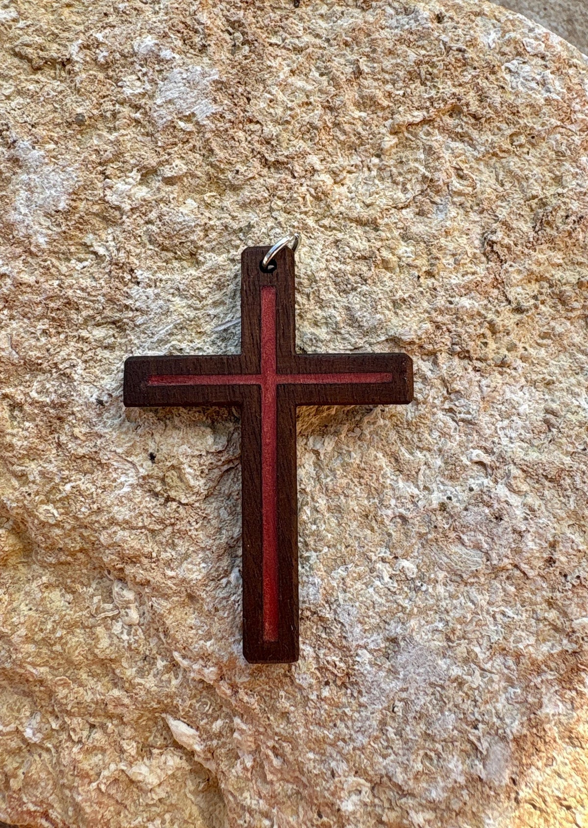 	Black walnut cross pendant with red resin inlay on textured tan rock