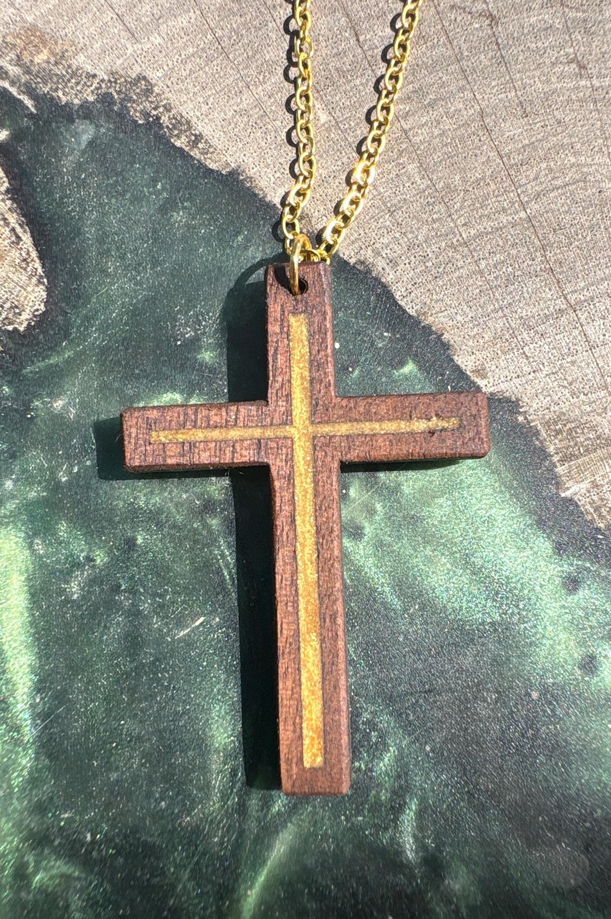 Close-up of gold resin-inlay walnut cross necklace on a green resin-and-wood surface