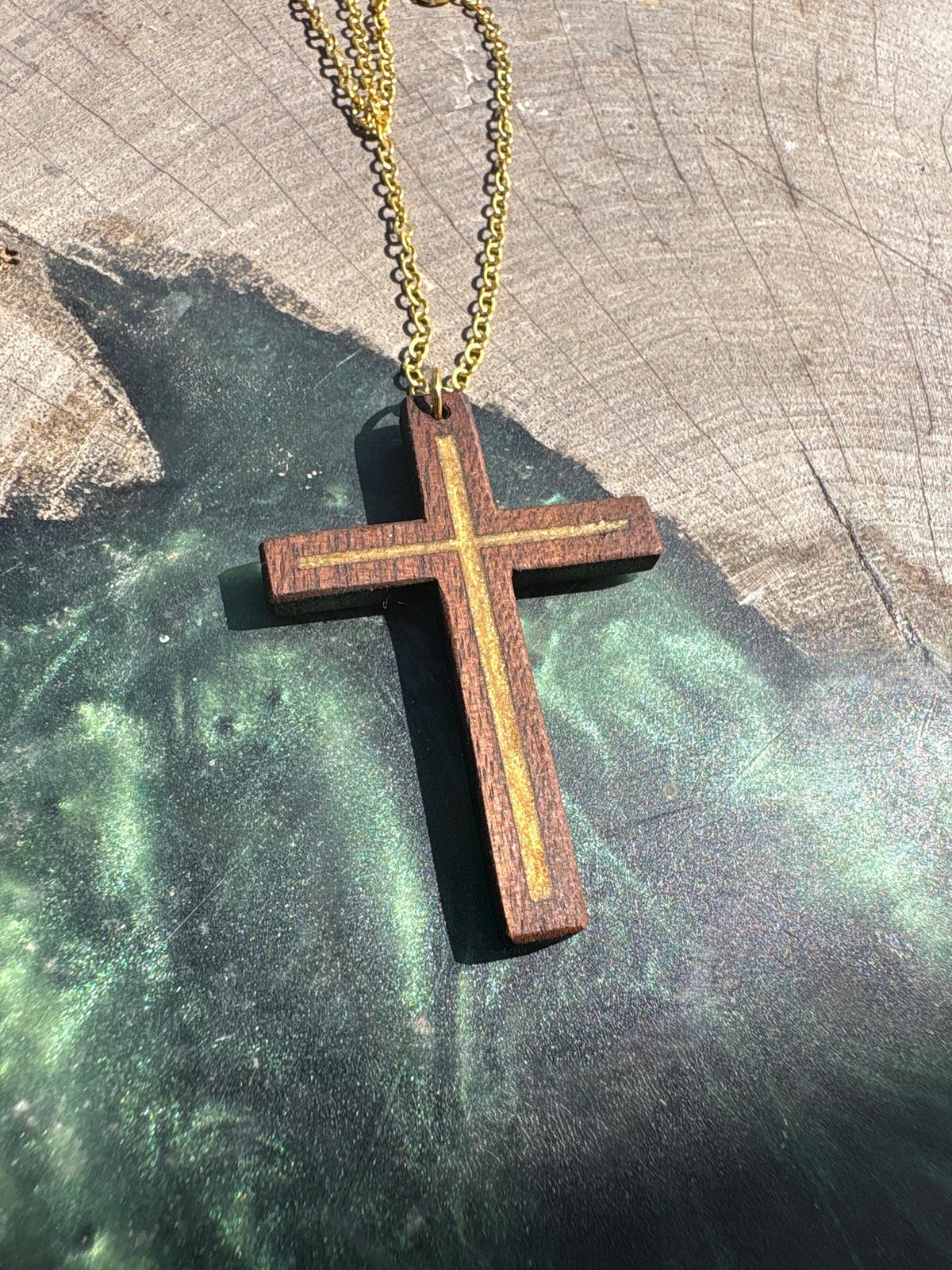 Gold resin-inlay walnut cross necklace and gold-colored chain displayed on wood and green resin
