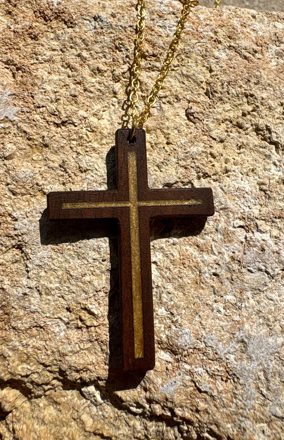 Black walnut cross necklace with gold resin inlay and gold-colored chain on textured tan rock