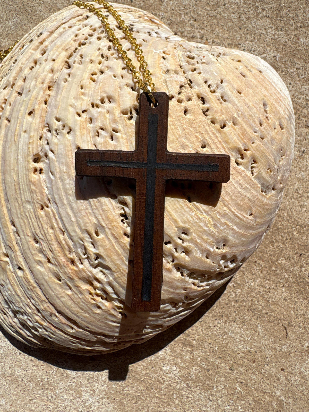 Black walnut cross necklace with blue resin inlay and gold-colored chain on a pale seashell