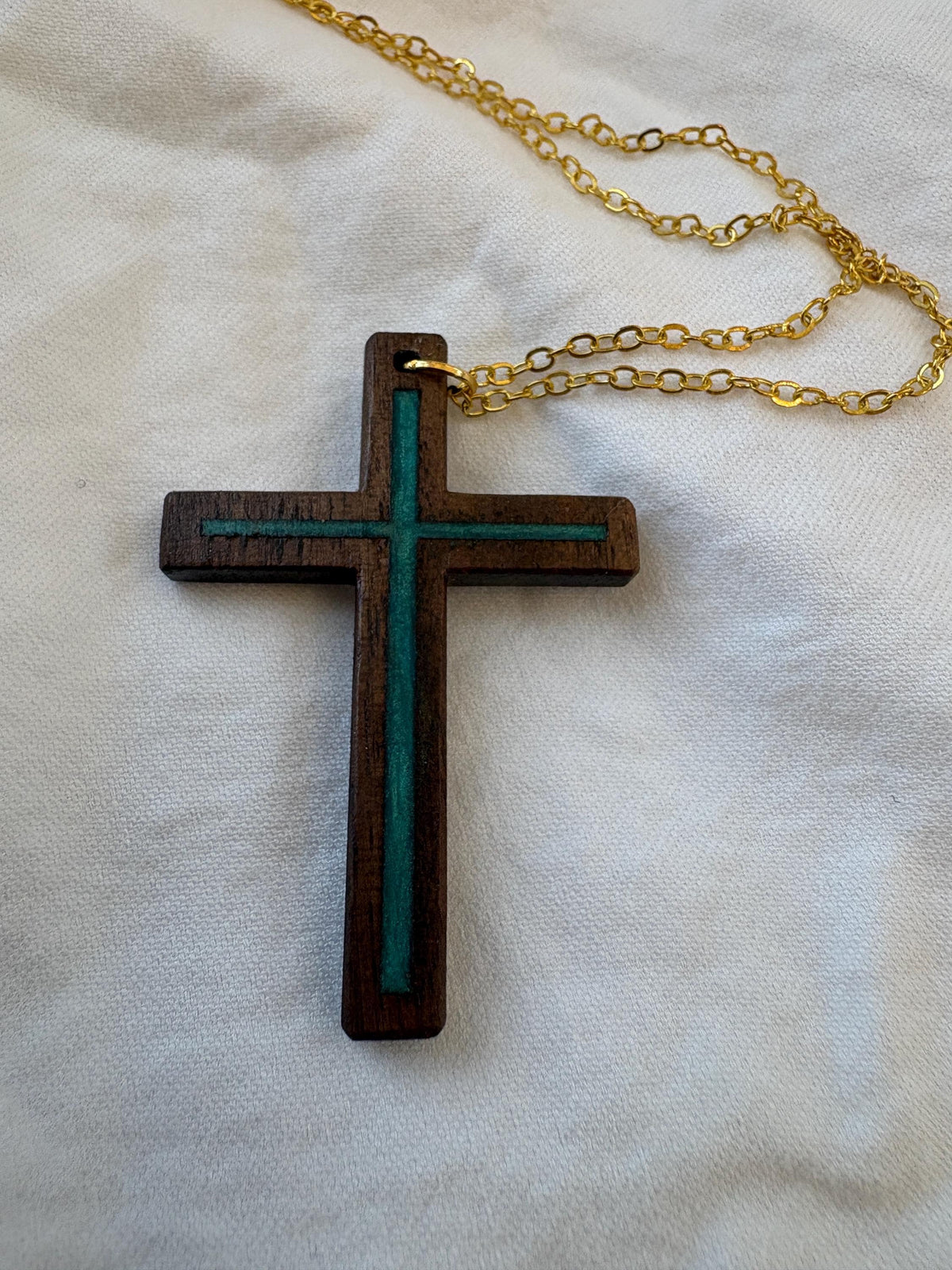 Black walnut cross necklace with turquoise resin inlay and gold-colored chain on white fabric