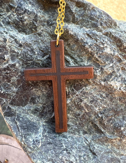 Black walnut cross necklace with dark blue resin inlay and gold-colored chain on dark rock