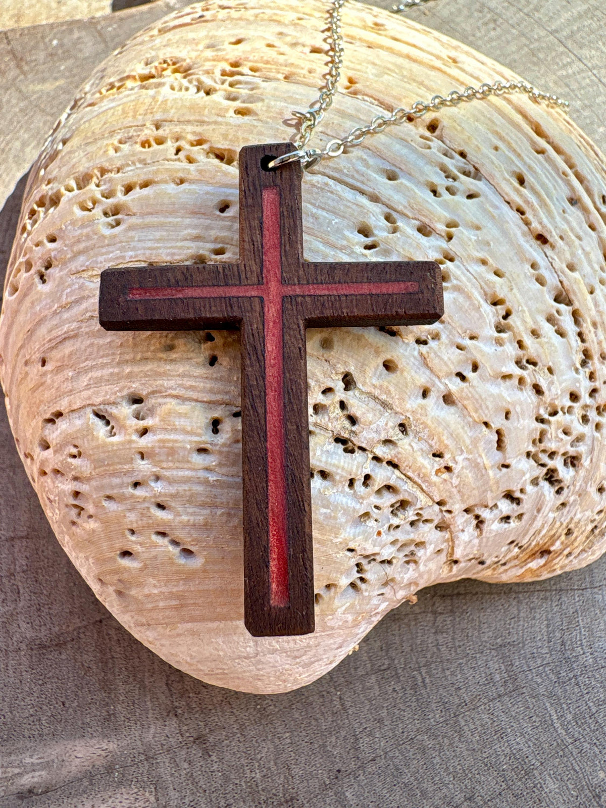 	Black walnut cross necklace with red resin inlay and silver-colored chain on a pale seashell