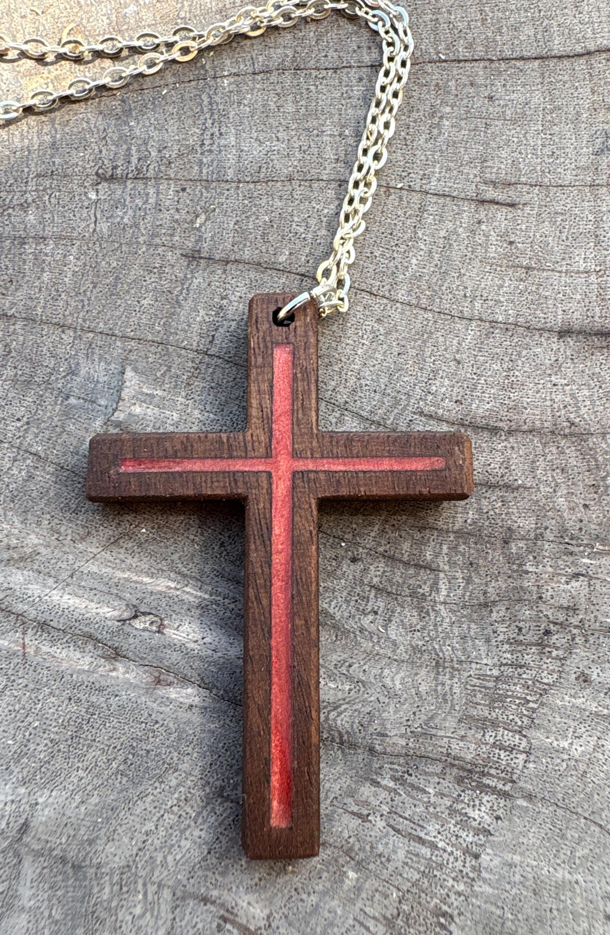 Red resin-inlay walnut cross necklace with silver-colored chain on a gray wood surface