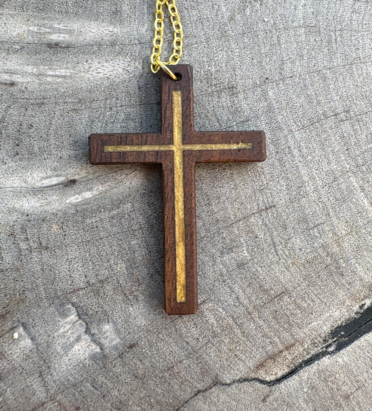 	Black walnut cross pendant with gold resin inlay and gold-colored chain on gray wood