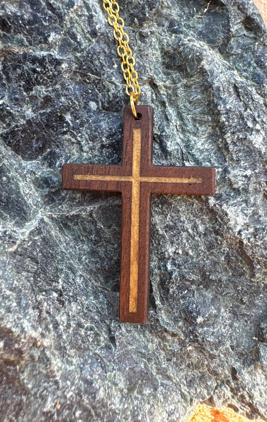 Black walnut cross necklace with gold resin inlay and gold-colored chain on dark rock