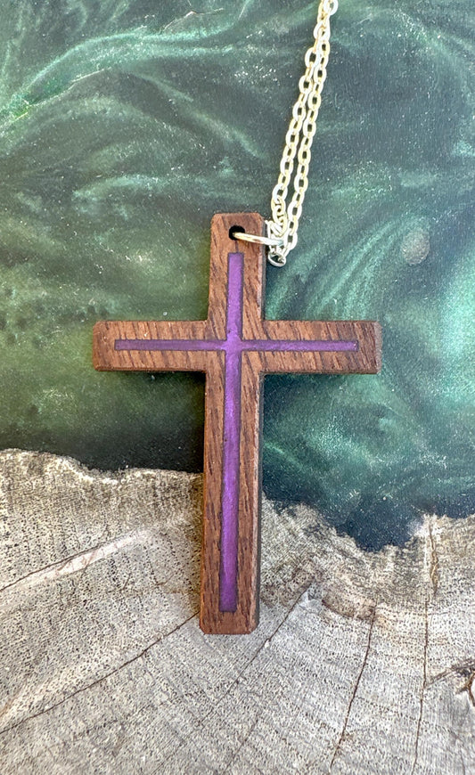Black walnut cross necklace with purple resin inlay and silver-colored chain on a green resin-and-wood surface